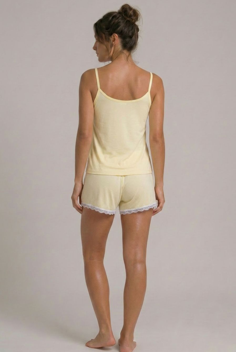 Modelo usando pijama feminino conjunto Veneza amarelo com blusa de alças, short e detalhe em renda branca em vista traseira